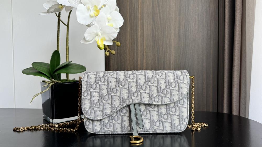 The saddle chain handbag series woc chain bag is carefully crafted from classic gray oblique floral fabric with a flip cover adorned with iconic lett